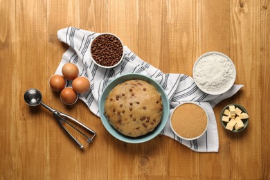 Bowl with dough and ingredients for cooking chocolate chip cookies on wooden table, flat lay