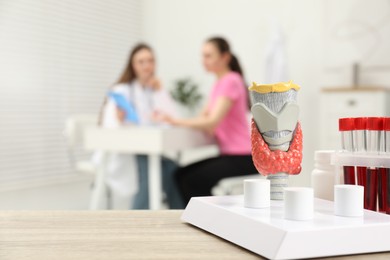 Photo of Endocrinologist examining patient at clinic, focus on model of thyroid gland and blood samples in test tubes