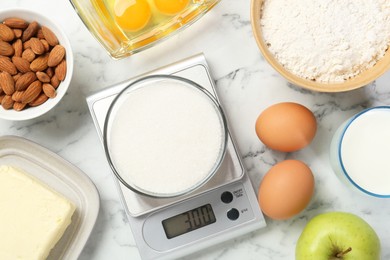 Photo of Flat lay composition of kitchen scale with bowl of sugar on white marble table