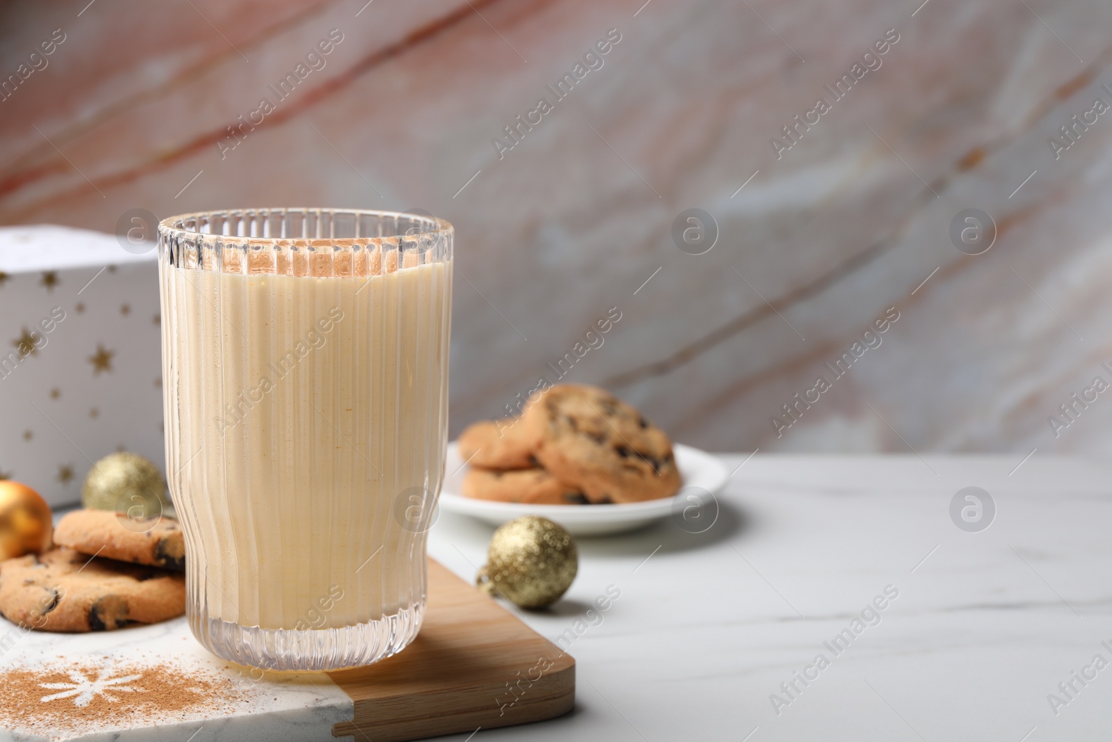 Photo of Glass of delicious eggnog with cinnamon and cookies on white table, space for text