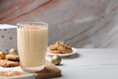 Glass of delicious eggnog with cinnamon and cookies on white table, space for text