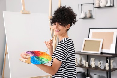 Photo of Young woman painting on easel with canvas in studio