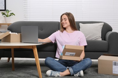 Photo of Happy woman using laptop while unpacking parcels at home. Online store