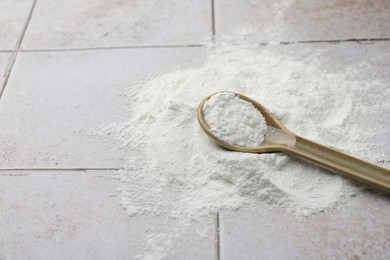 Pile of baking powder and spoon on light tiled table, closeup. Space for text