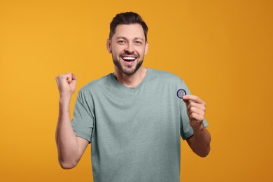 Photo of Excited man holding condom on orange background