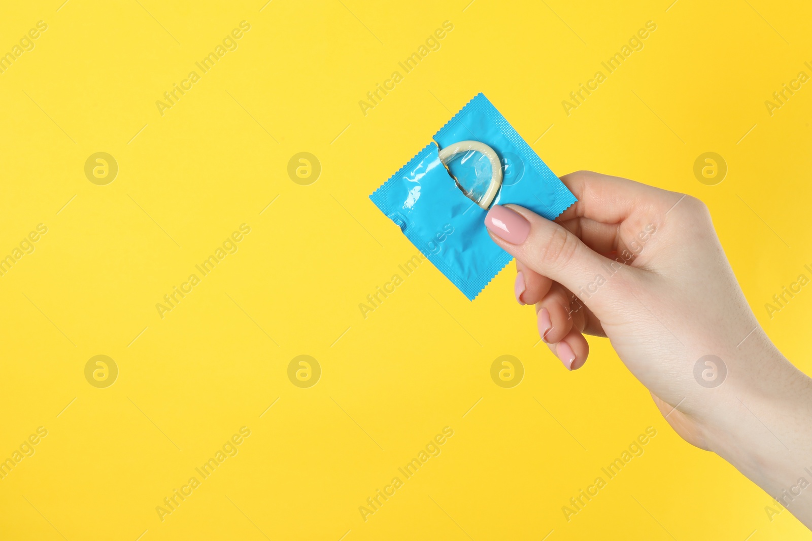 Photo of Woman holding condom on yellow background, closeup. Space for text