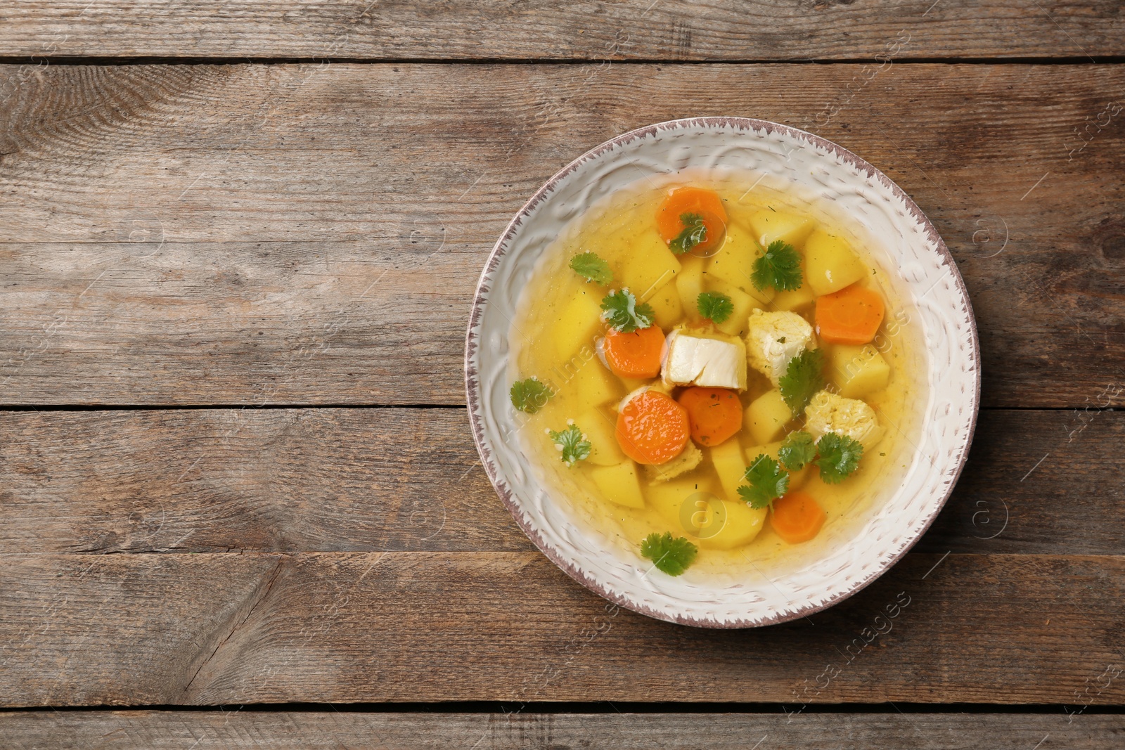 Photo of Homemade chicken soup served on wooden background, top view with space for text