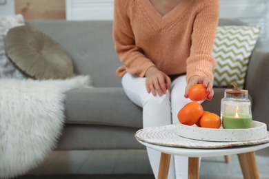 Photo of Young woman taking tangerine from table in living room, closeup