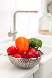 Photo of Fresh clean vegetables in colander on countertop near sink