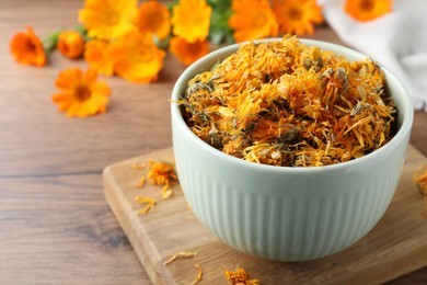 Photo of Bowl of dry calendula flowers on wooden table. Space for text