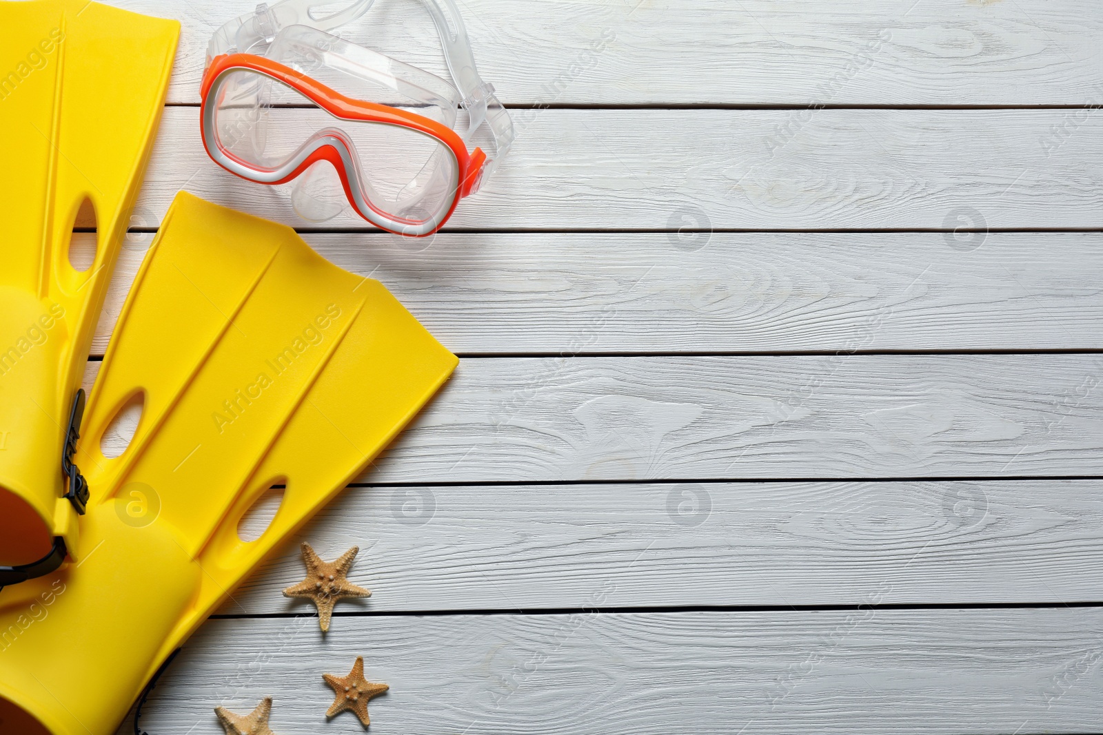 Photo of Goggles, flippers and starfishes on light wooden background, flat lay with space for text. Beach objects