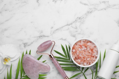 Flat lay composition with gua sha stone and face roller on white marble table. Space for text