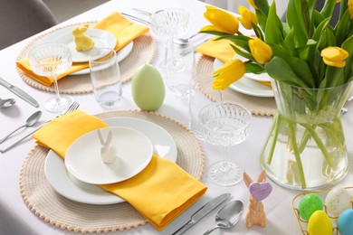 Festive table setting with glasses, painted eggs and vase of tulips. Easter celebration