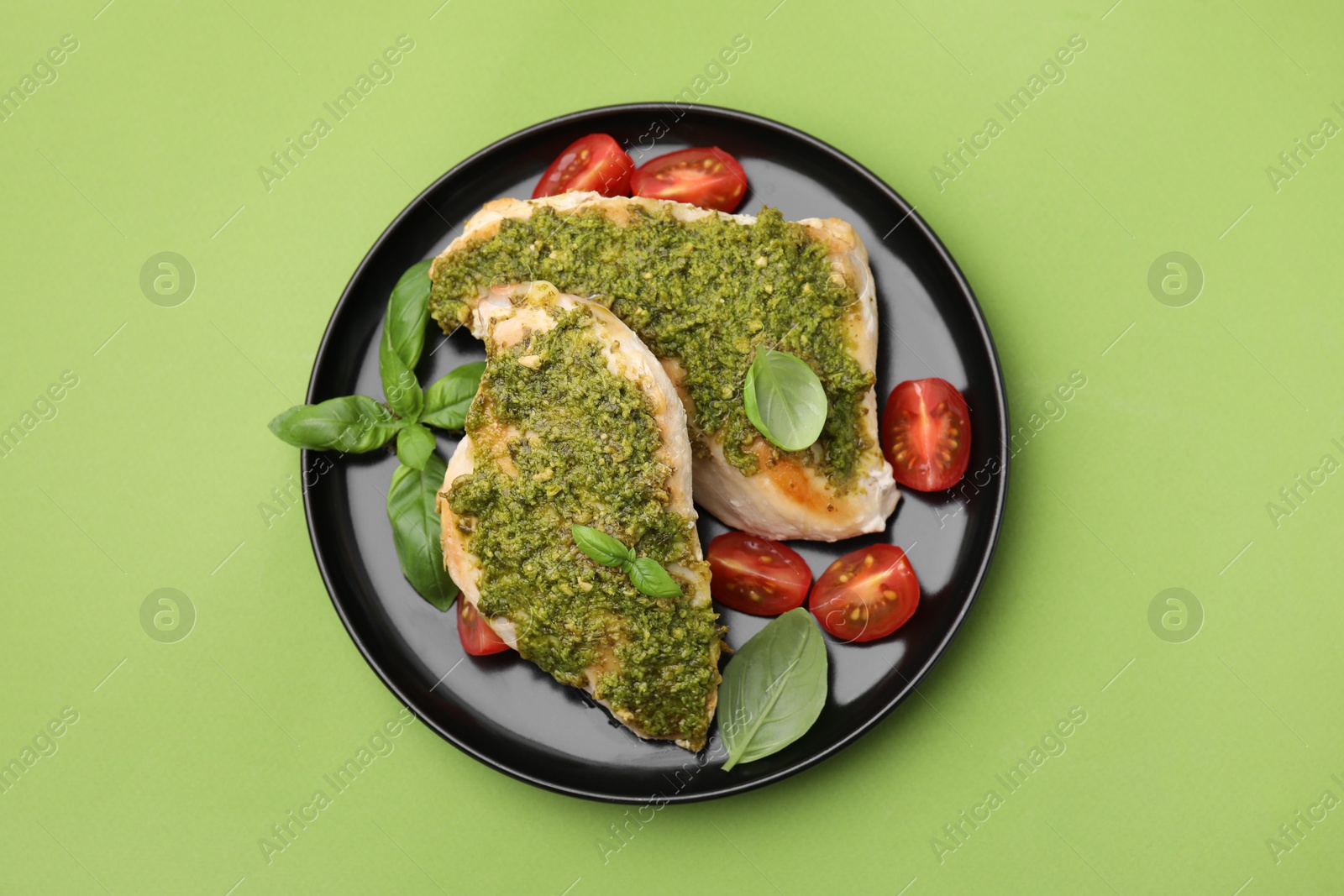 Photo of Delicious chicken breasts with pesto sauce, tomatoes and basil on light green table, top view