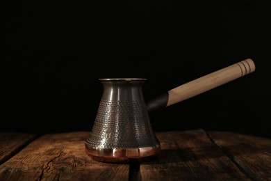 Photo of Beautiful copper turkish coffee pot on wooden table against dark background