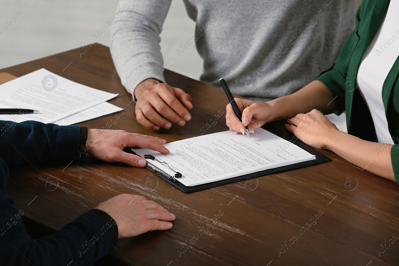 Photo of Notary helping couple with paperwork at wooden table, closeup