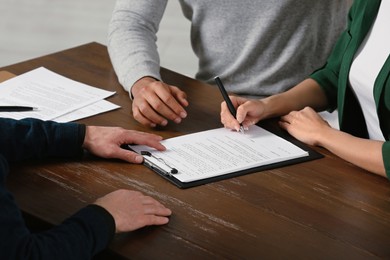 Notary helping couple with paperwork at wooden table, closeup