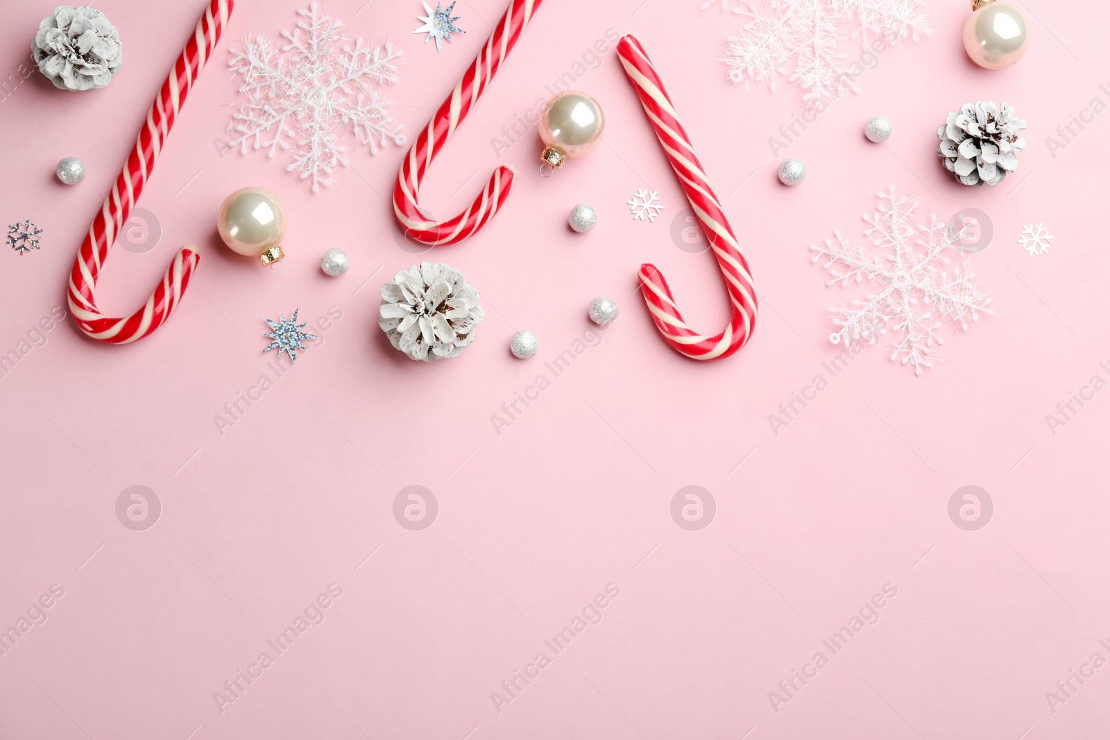 Photo of Flat lay composition with candy canes and Christmas decor on pink background. Space for text