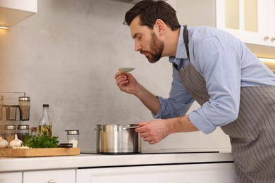 Photo of Man tasting delicious soup with spoon in kitchen