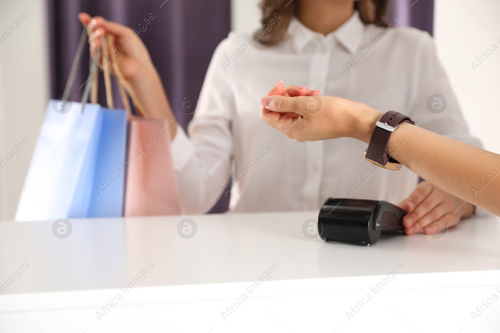 Photo of Woman using terminal for contactless payment with smart watch in shop, closeup