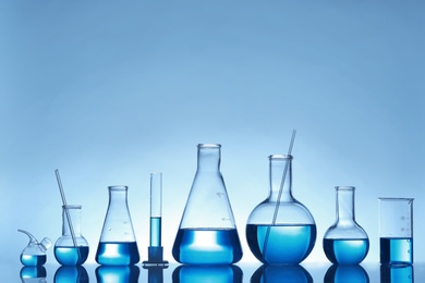 Photo of Laboratory glassware with liquid on table against color background. Chemical analysis