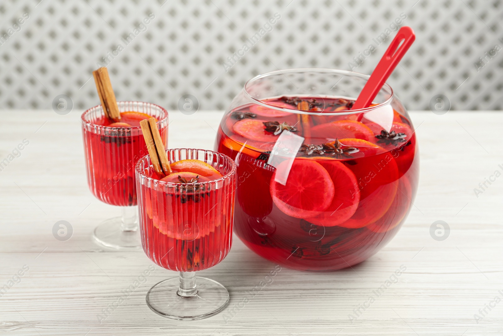 Photo of Glasses and bowl of delicious aromatic punch drink on white wooden table