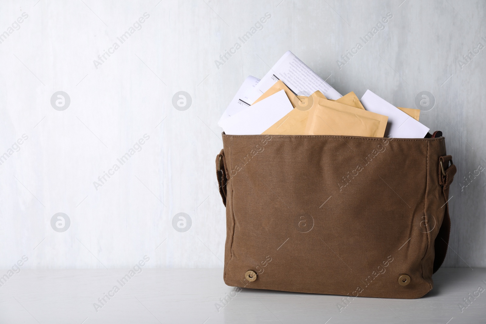 Photo of Postman's bag full of letters and newspapers on white wooden background. Space for text