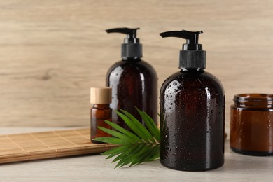 Shampoo bottles, essential oil, hair mask and green leaf on white wooden table