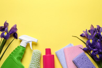 Spring cleaning. Detergents, flowers, sponge, brush and rags on yellow background, flat lay. Space for text