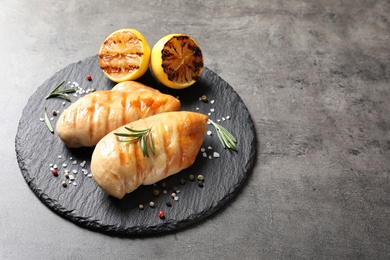 Photo of Slate plate with grilled chicken breasts and lemon on grey table. Space for text