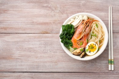 Photo of Delicious ramen with shrimps and egg in bowl and chopsticks on wooden table, top view with space for text. Noodle soup