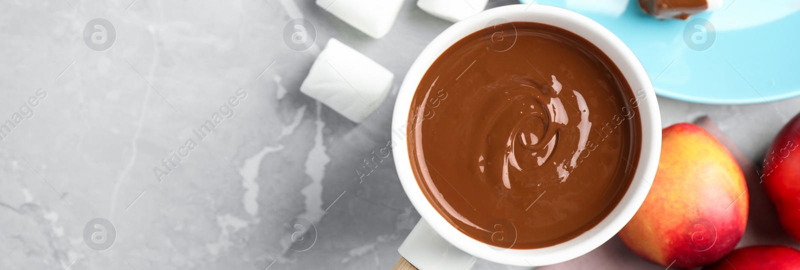 Image of Fondue pot and marshmallow dipped into milk chocolate on light grey table, flat lay with space for text. Banner design