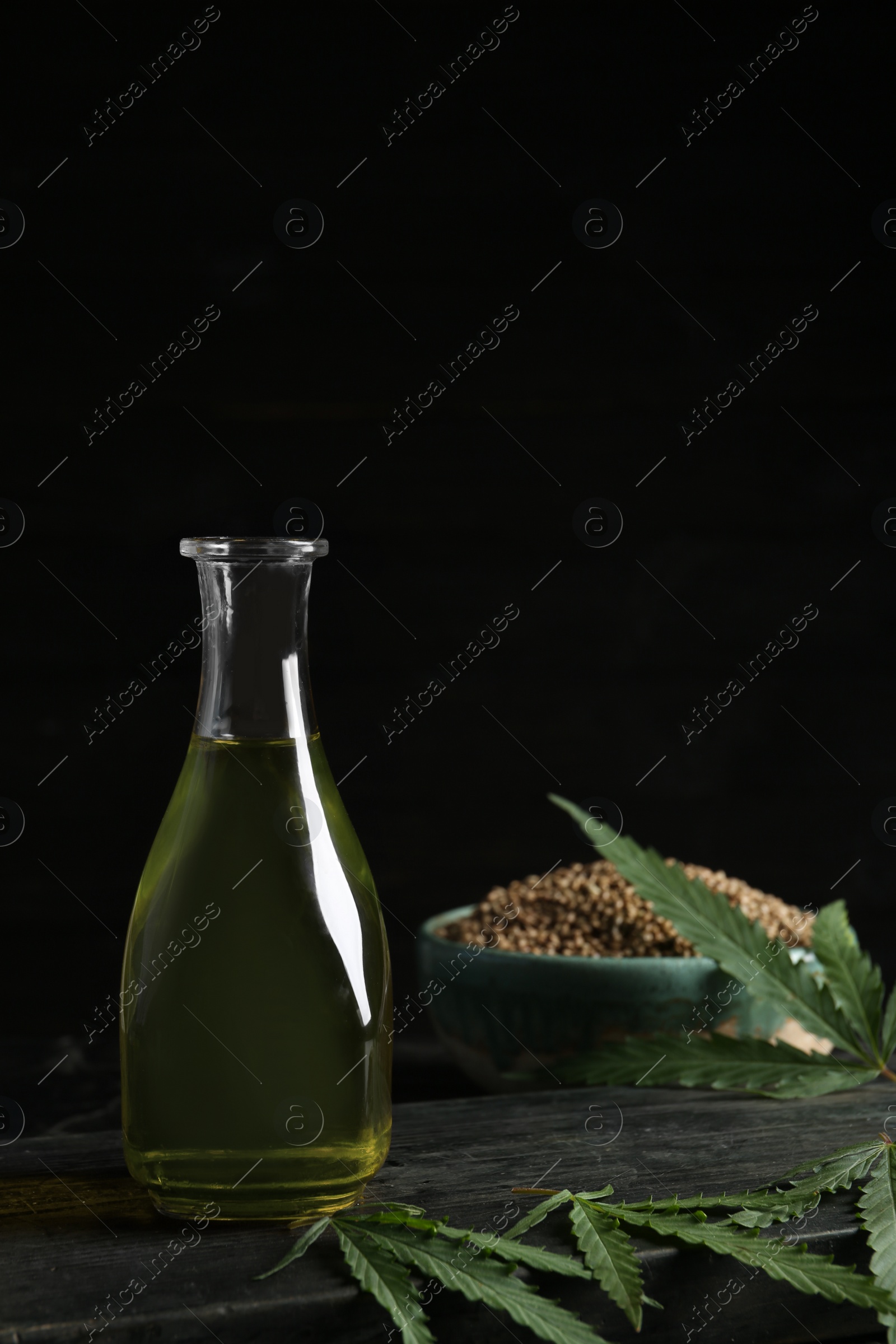 Photo of Bottle with hemp oil and fresh leaves on dark table. Space for text