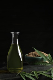 Photo of Bottle with hemp oil and fresh leaves on dark table. Space for text