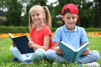 Photo of Cute little children reading books on green grass in park