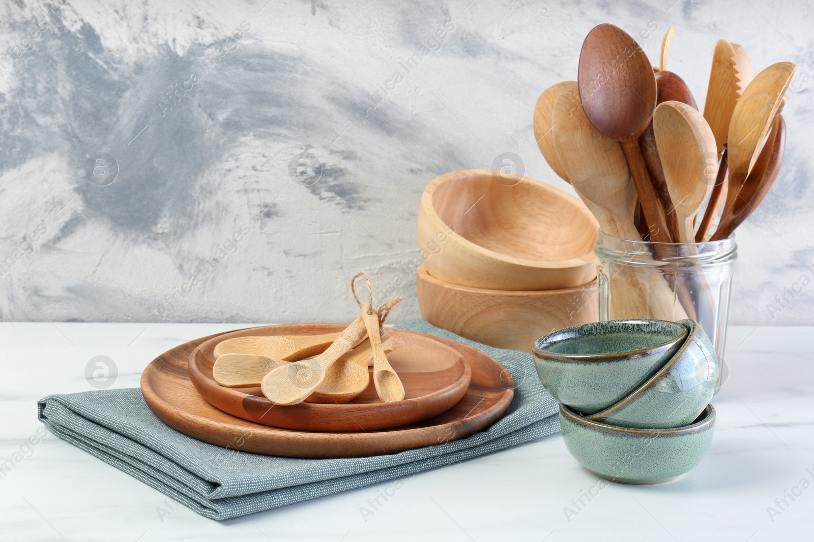 Photo of Different dishware and utensils on white marble table against textured wall