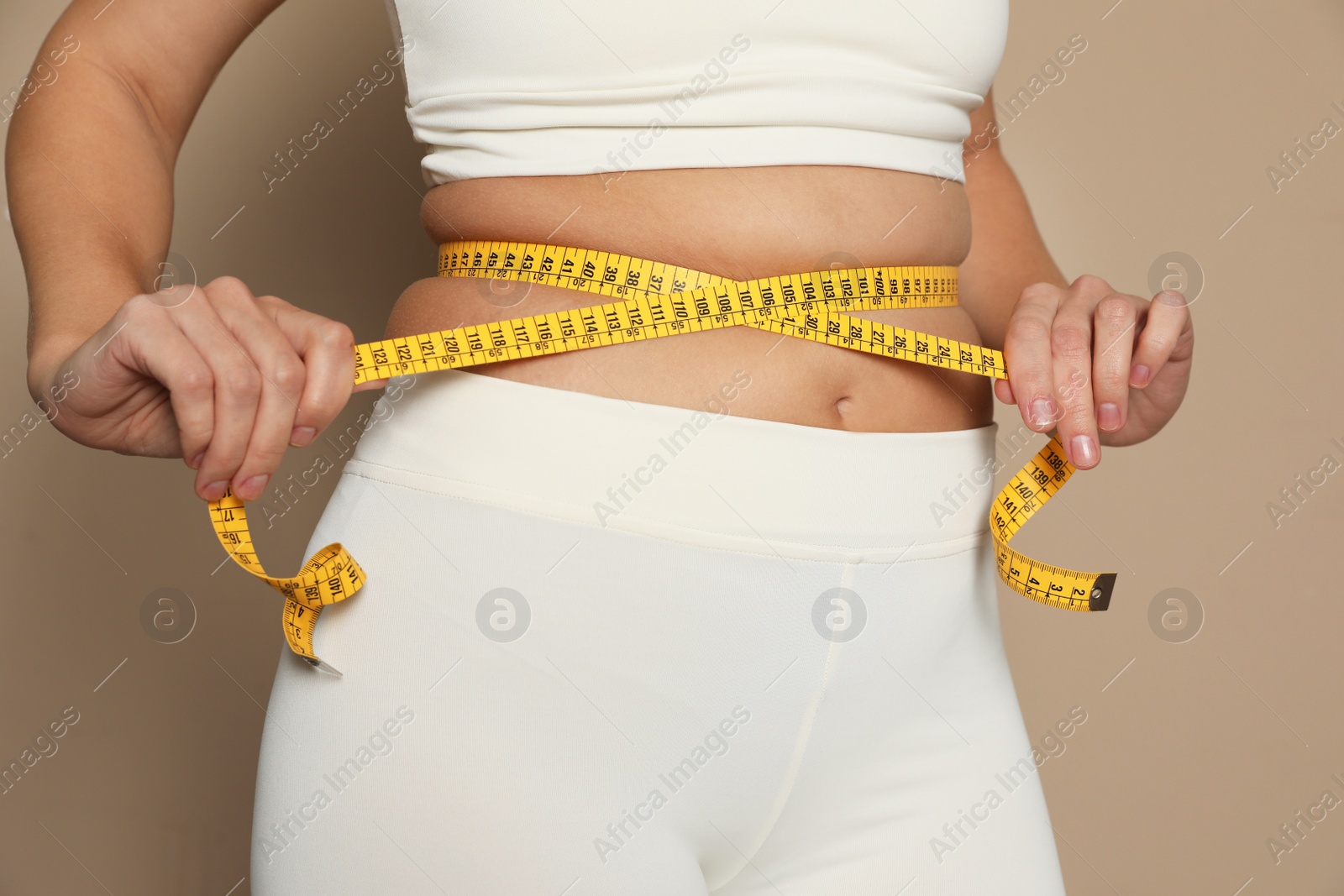 Photo of Woman measuring waist with tape on beige background, closeup