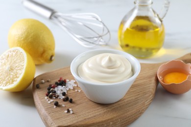 Photo of Tasty mayonnaise sauce in bowl, ingredients and spices on white table, closeup