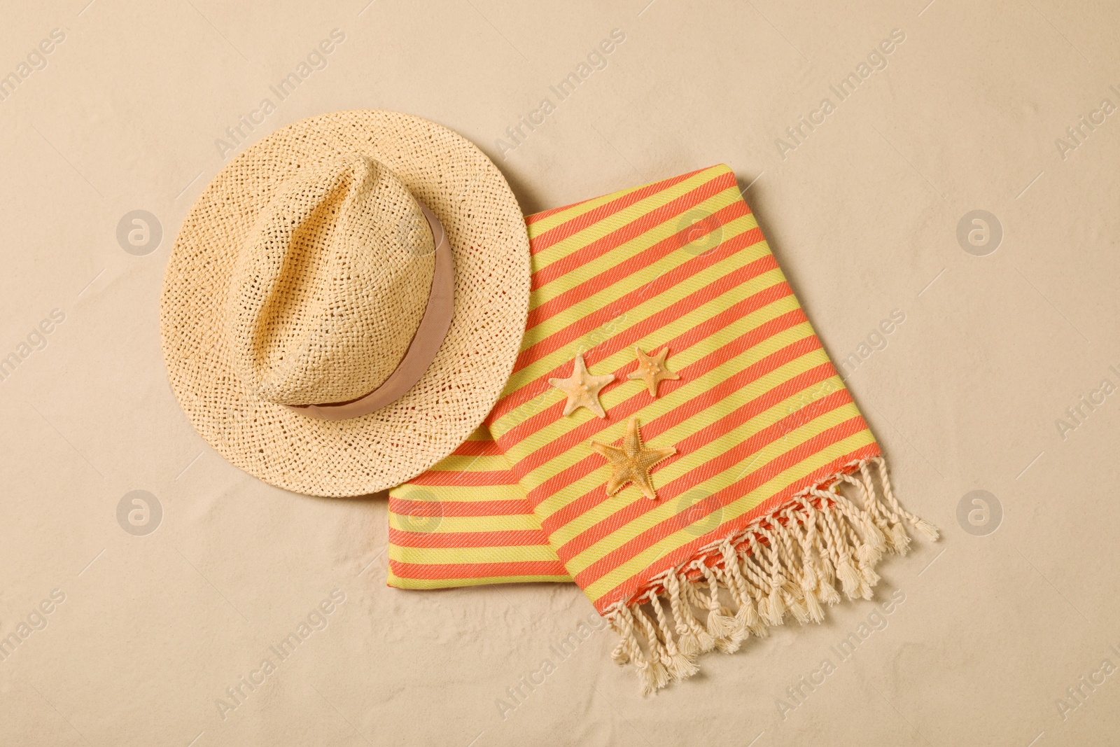 Photo of Beach towel, hat and starfishes on sand, flat lay