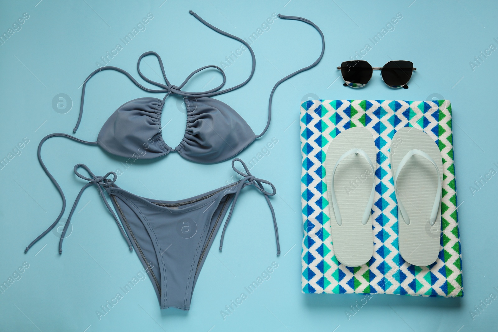 Photo of Stylish bikini and beach accessories on light blue background, flat lay