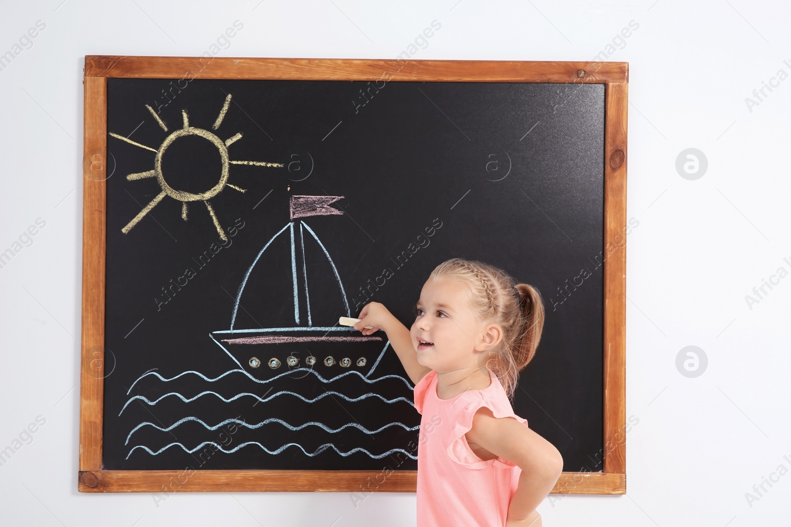 Photo of Little child drawing ship with colorful chalk on blackboard