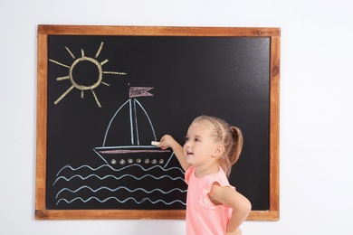 Little child drawing ship with colorful chalk on blackboard