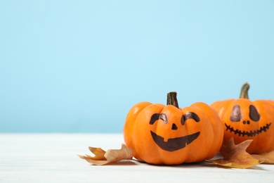 Photo of Pumpkins with scary faces and fallen leaves on white wooden table, space for text. Halloween decor