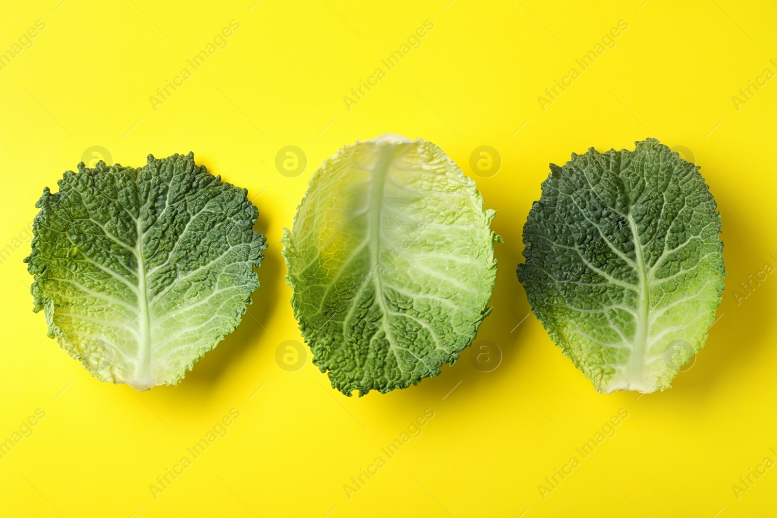 Photo of Fresh savoy cabbage leaves on yellow background, flat lay