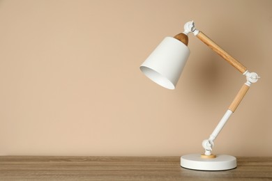 Photo of Stylish modern desk lamp on wooden table near beige wall, space for text