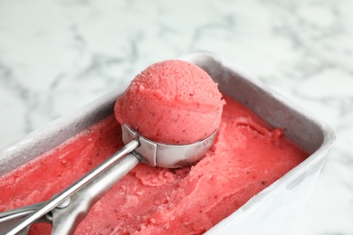 Photo of Container with delicious pink ice cream and scoop on marble table, closeup