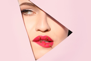 Photo of View of beautiful young woman with creative lips makeup through cutout in color paper