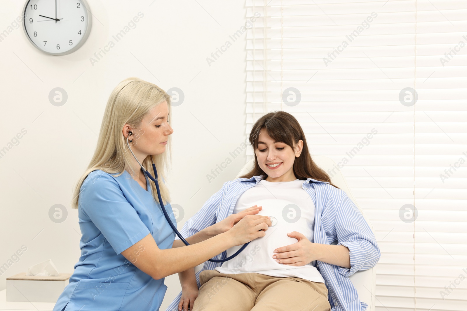 Photo of Pregnancy checkup. Doctor with stethoscope listening baby's heartbeat in patient's tummy in clinic