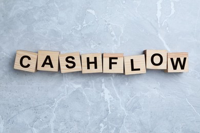 Image of Wooden cubes with phrase Cash FLow on light grey marble background, flat lay