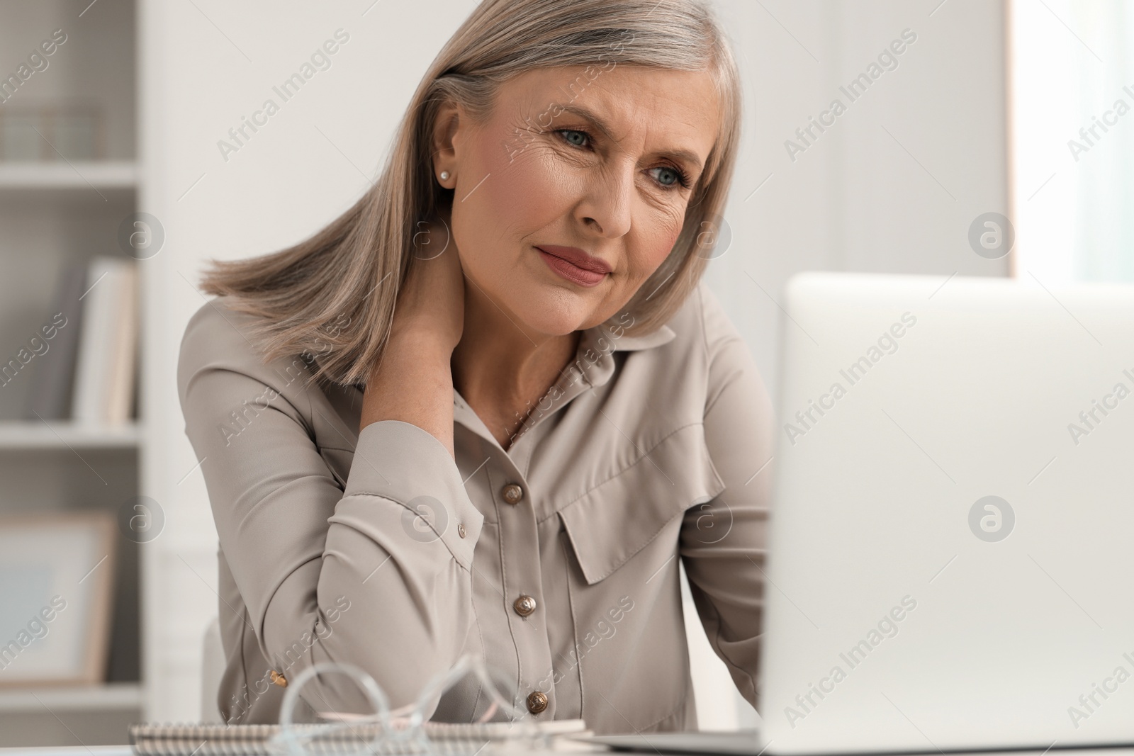 Photo of Woman suffering from neck pain at workplace in room